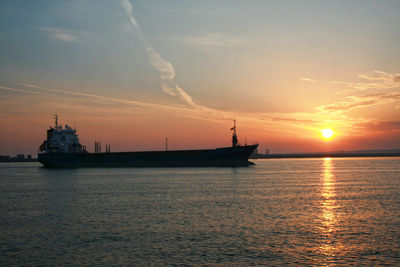 Scenic view of a container ship entering harbor against sky during sunrise