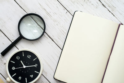 Directly above shot of clock with magnifying glass and diary on wooden table