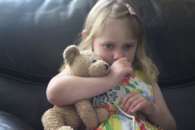 Close-up of cute girl holding teddy bear while sitting on sofa at home