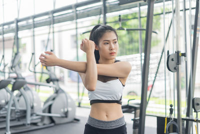 Young woman stretching arms while exercising at gym