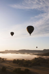 Hot air balloons flying over landscape against sky during sunset