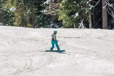 Full length of woman snowboarding against trees