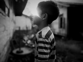 Side view of boy standing in yard against bright sun