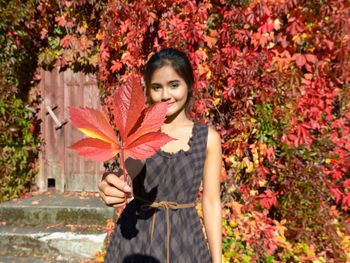 Portrait of young woman holding maple leaf during autumn