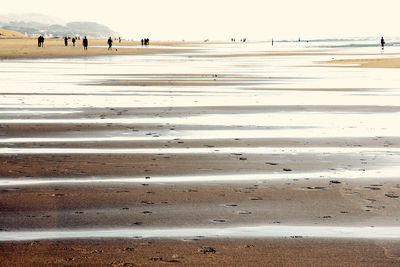 People walking on beach against sky during winter