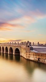 Arch bridge over river against sky during sunset