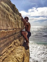 Man standing on rock by sea against sky