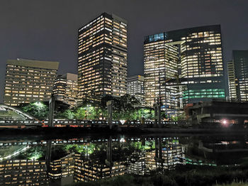 Illuminated buildings by river against sky in city at night