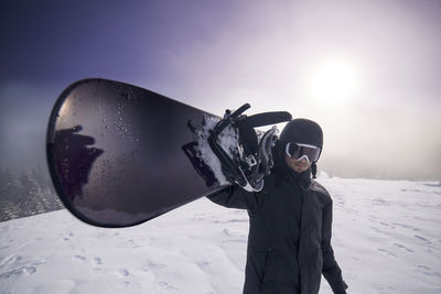 Portrait of man carrying ski on snowy landscape against sky