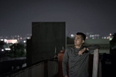 Young man standing at building terrace against sky