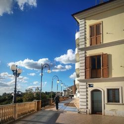 Man walking on street by building against sky