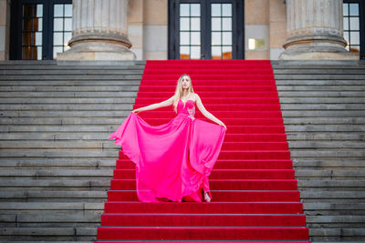 Female model wearing pink evening gown while standing on steps