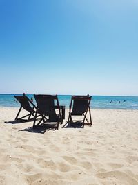 Deck chairs on beach against clear blue sky