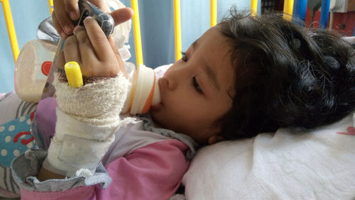 Cute injured girl using phone while lying on hospital bed