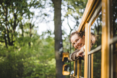 Smiling woman looking through caravan window during camping in forest