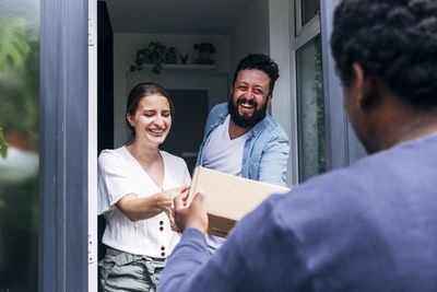 Cheerful couple receiving package from delivery person at entrance of house