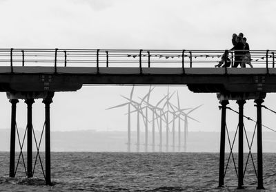 People on pier over sea against sky