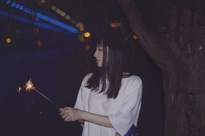 Woman holding lit sparkler at night