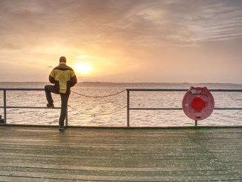 Rear view of man standing by sea against sky during sunset