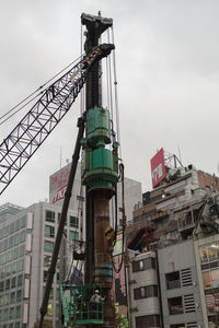 Low angle view of crane by building against sky