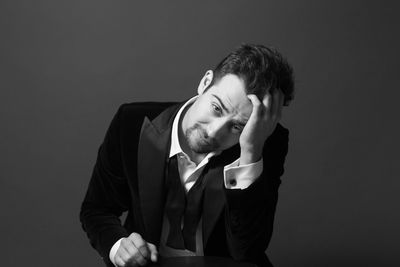 Portrait of handsome young man with head in hands sitting against black background