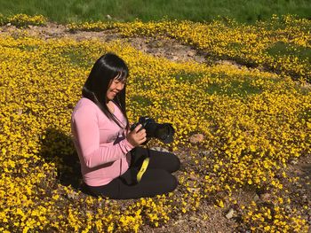 Young woman using mobile phone while sitting on yellow flowers