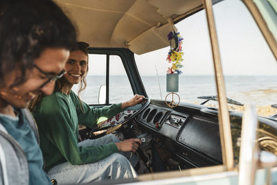 Smiling woman talking with male friend while sitting in camping van during road trip