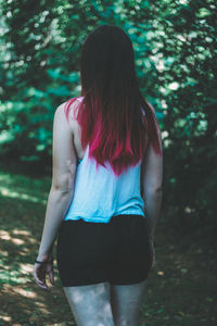 Rear view of young woman standing against trees