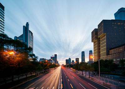 City street and modern buildings against sky at dusk