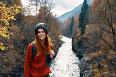 Portrait of smiling young woman standing by trees during autumn