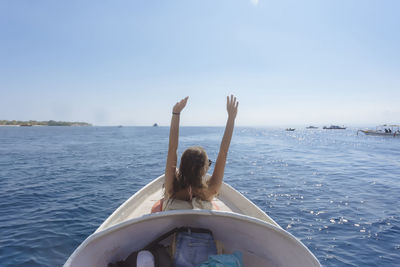 Rear view of woman with arms raised standing in boat on sea against clear sky