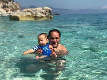 Portrait of father carrying son while swimming in sea