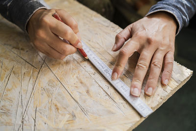 Cropped hands of female carpenter marking on plank with pencil