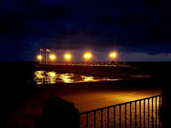 Illuminated bridge over river against sky at night