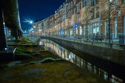 Illuminated street by buildings in city at night