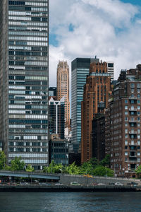 Modern buildings by river against sky in city