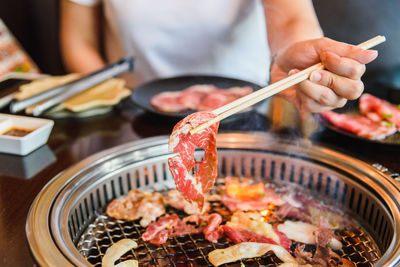 Midsection of woman holding meat with chopsticks at restaurant