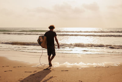 Rear view of man carrying surfboard walking at beach