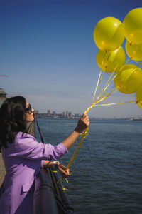 Rear view of woman holding umbrella at sea against clear sky