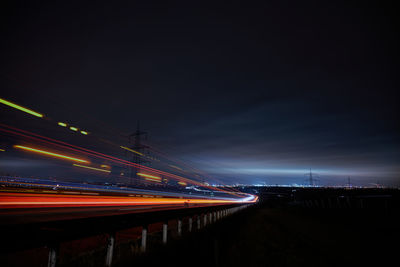 Illuminated light trails on road against sky at night