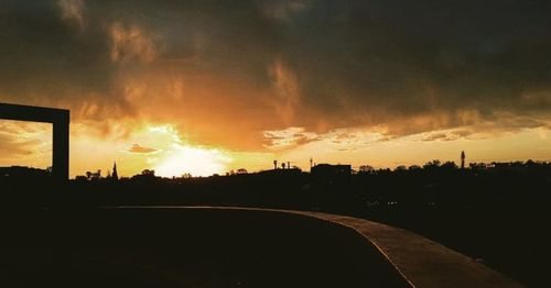 Silhouette city against dramatic sky during sunset
