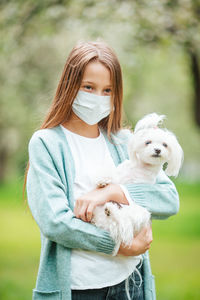 Smiling girl wearing mask holding dog standing at park