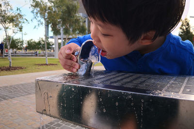 Close-up of cute thirsty boy drinking water from fountain