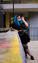 Young woman with blue hair standing by retaining wall