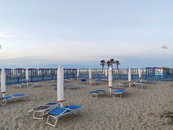 Deck chairs on beach against sky during sunset