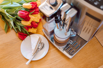 Cup of coffee with milk, piece of cake and tulips flowers on wooden kitchen table. freshly 