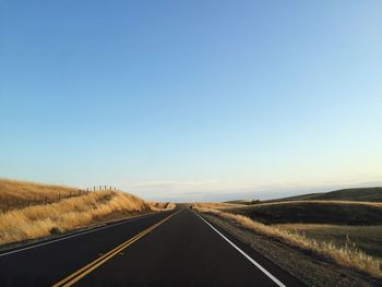 Empty road by field against clear sky