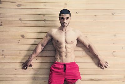 Shirtless man exercising against wooden wall