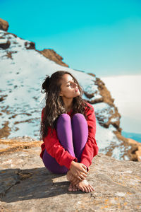 Full length of woman sitting on rocky mountain