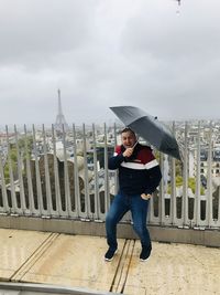 Portrait of cheerful man holing umbrella while standing on footpath against sky